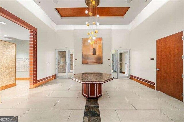 hallway with french doors, light tile patterned floors, a high ceiling, and a raised ceiling