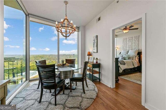 dining space with ceiling fan with notable chandelier, wood-type flooring, and a healthy amount of sunlight