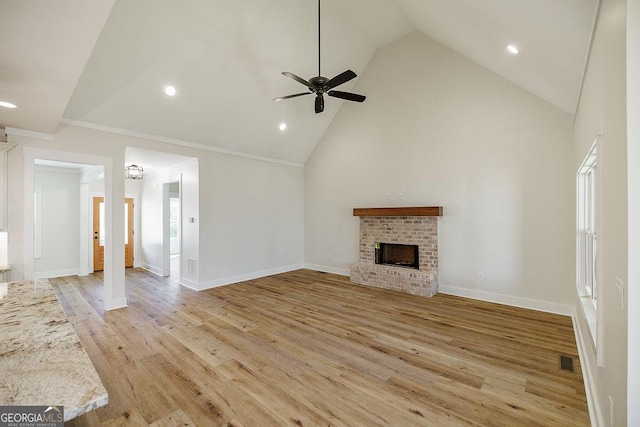 unfurnished living room featuring a brick fireplace, light hardwood / wood-style flooring, ceiling fan, high vaulted ceiling, and crown molding