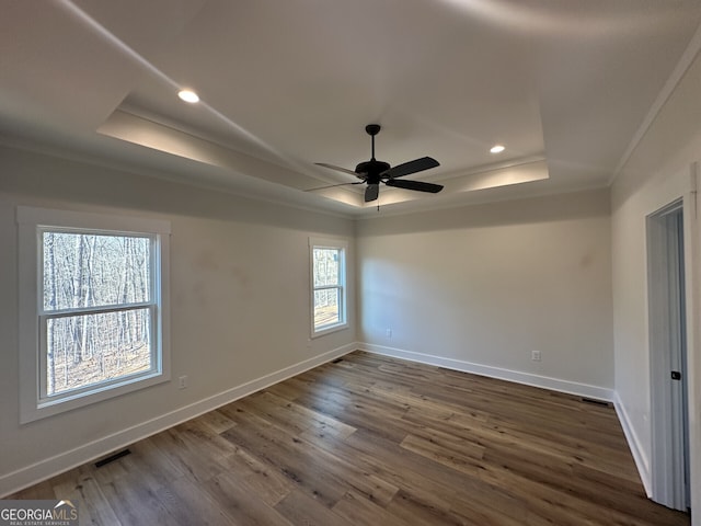 spare room with dark wood-type flooring, ceiling fan, crown molding, and a raised ceiling