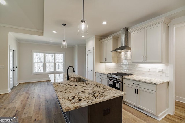 kitchen with high end stainless steel range oven, wall chimney exhaust hood, pendant lighting, sink, and a kitchen island with sink