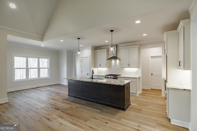 kitchen featuring a center island with sink, wall chimney exhaust hood, white cabinets, pendant lighting, and sink