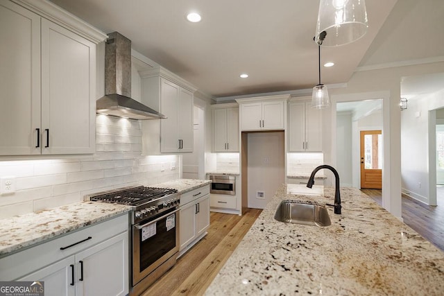 kitchen featuring sink, light stone counters, stainless steel range, decorative light fixtures, and wall chimney exhaust hood