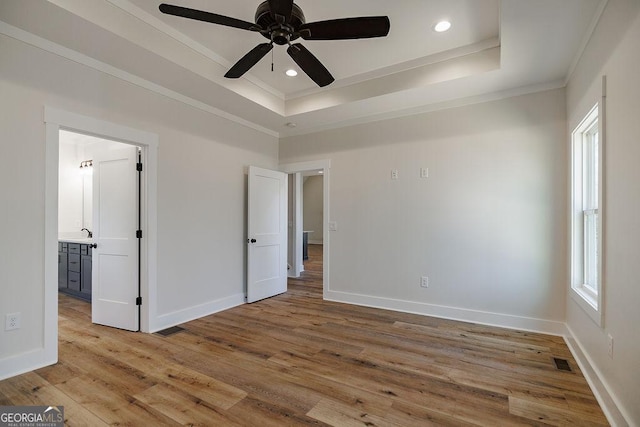 unfurnished bedroom featuring a tray ceiling, crown molding, and light hardwood / wood-style flooring