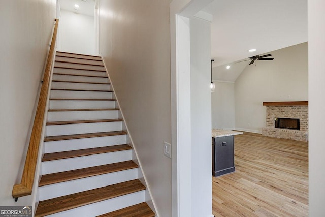 stairs with a fireplace, ceiling fan, vaulted ceiling, and hardwood / wood-style flooring