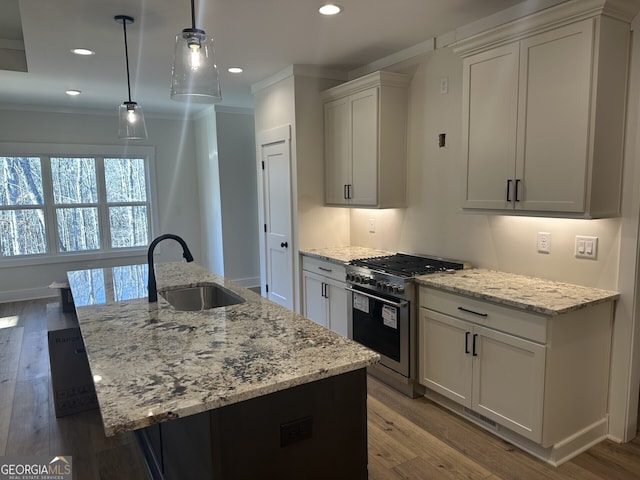 kitchen with sink, gas range, hanging light fixtures, an island with sink, and white cabinets