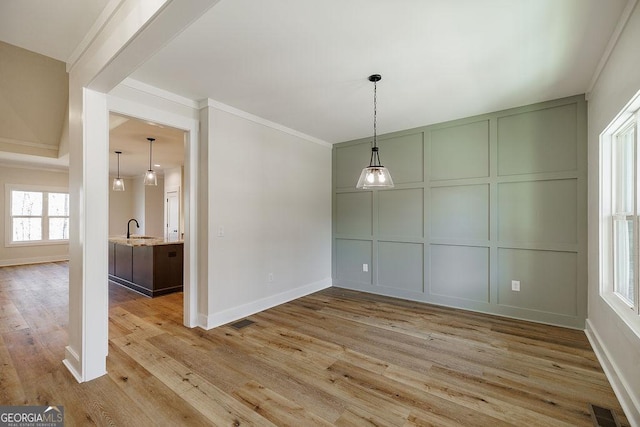 unfurnished dining area with sink, light hardwood / wood-style floors, and crown molding