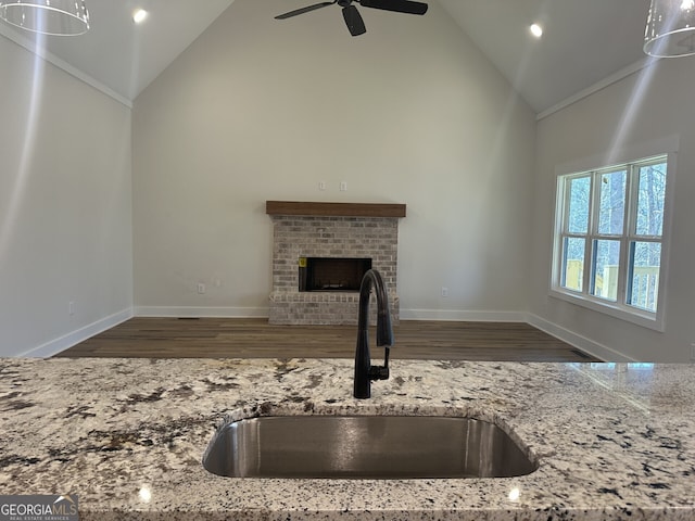 kitchen with dark wood-type flooring, sink, high vaulted ceiling, a fireplace, and light stone countertops