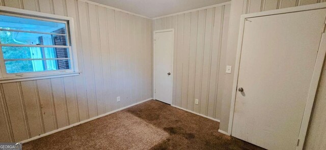 unfurnished bedroom with wood walls, ornamental molding, and dark colored carpet