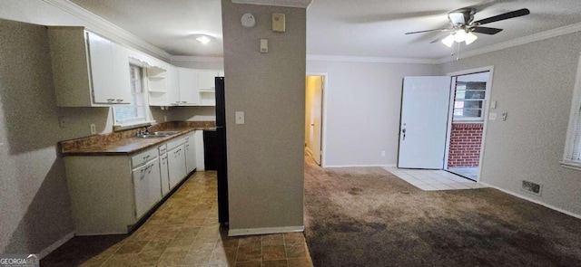 kitchen with ornamental molding, carpet, sink, white cabinetry, and ceiling fan