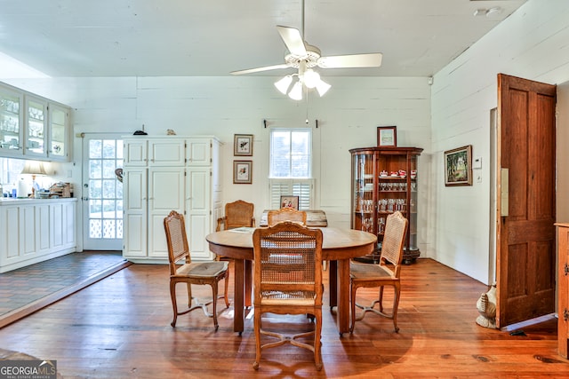 dining area featuring ceiling fan, hardwood / wood-style flooring, and wood walls