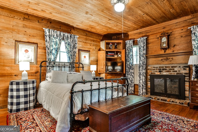 bedroom featuring wood walls, wooden ceiling, a brick fireplace, and hardwood / wood-style floors