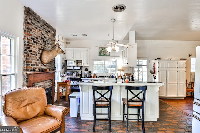 kitchen with ceiling fan, white cabinetry, a kitchen bar, a fireplace, and sink