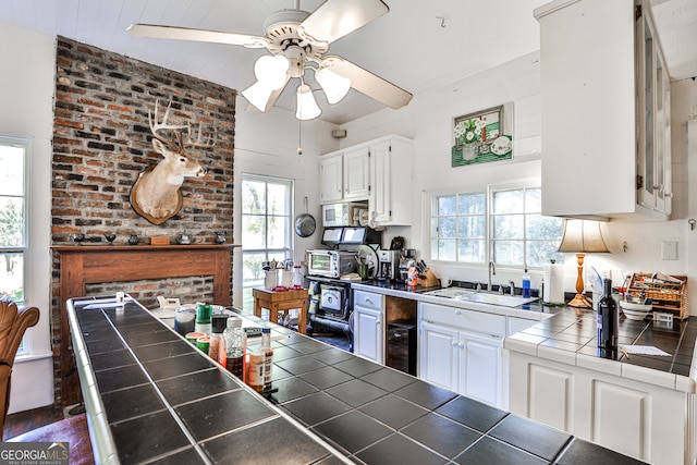 kitchen featuring ceiling fan, white cabinetry, tile counters, sink, and brick wall