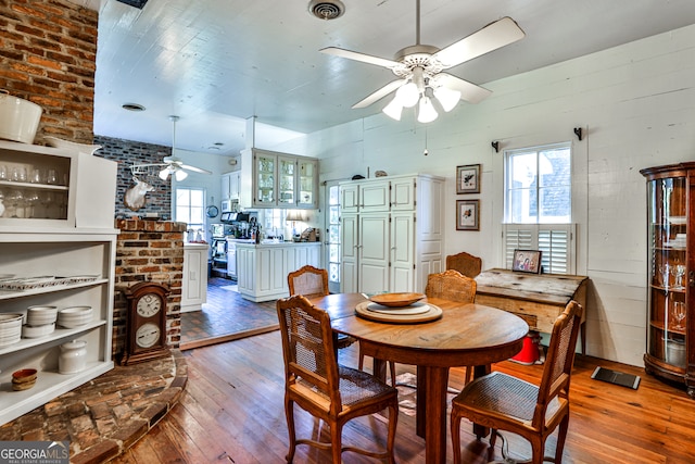 dining room featuring ceiling fan, brick wall, and wood-type flooring