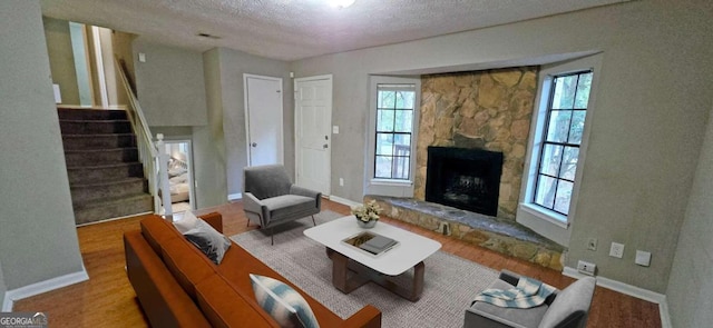 living room featuring a stone fireplace, light hardwood / wood-style flooring, a textured ceiling, and a healthy amount of sunlight