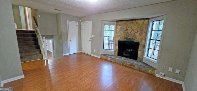 unfurnished living room with a textured ceiling, stairway, a wealth of natural light, and wood finished floors