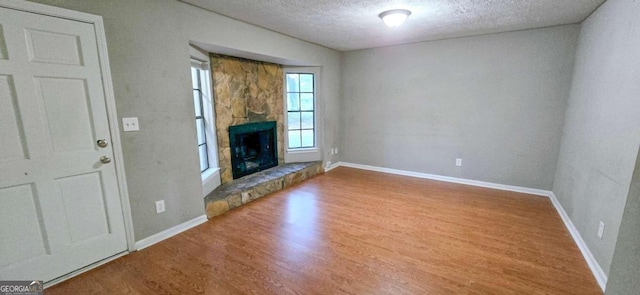 unfurnished living room featuring a fireplace, a textured ceiling, wood finished floors, and baseboards