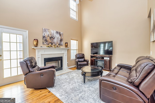 living room featuring a towering ceiling, a tiled fireplace, and light wood-type flooring