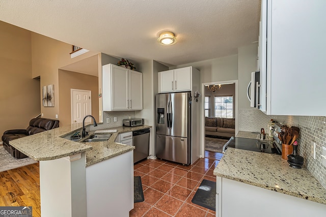 kitchen featuring light stone countertops, appliances with stainless steel finishes, sink, kitchen peninsula, and white cabinets