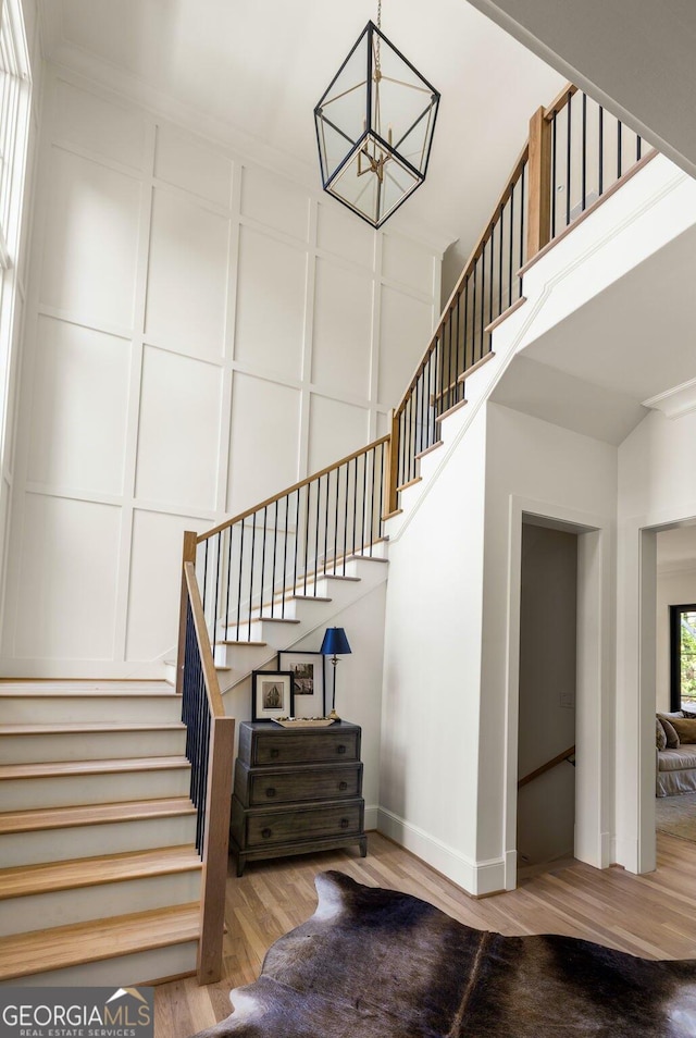 stairs featuring a notable chandelier, hardwood / wood-style flooring, and a towering ceiling