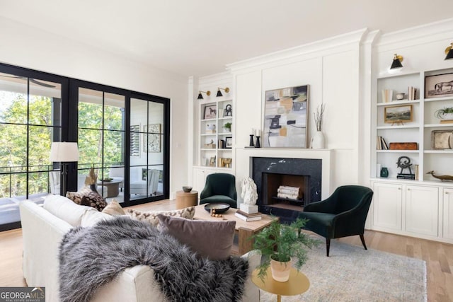 sitting room featuring crown molding, a fireplace, built in features, and light wood-type flooring