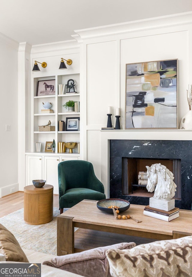 living area with hardwood / wood-style floors, crown molding, a premium fireplace, and built in shelves