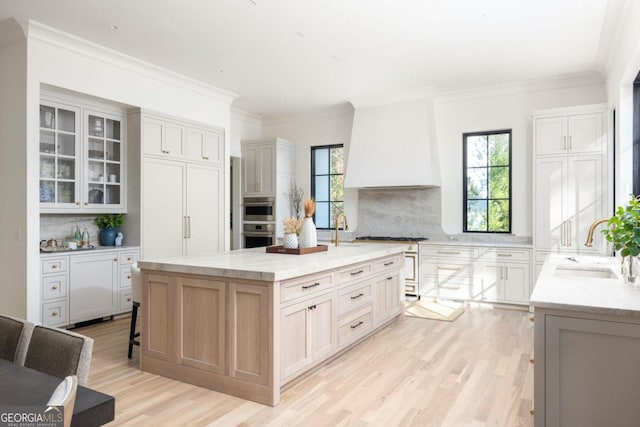 kitchen featuring a large island, sink, backsplash, and custom range hood