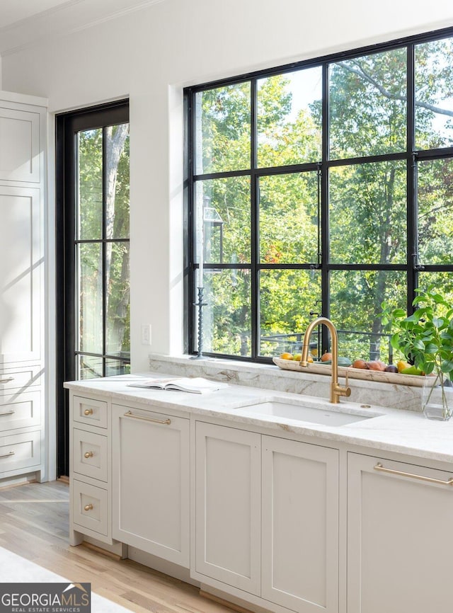 kitchen with light stone countertops, sink, white cabinets, and light hardwood / wood-style flooring