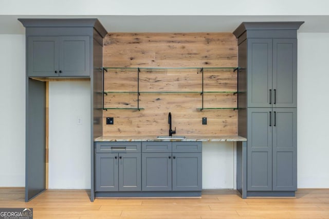 bar featuring light stone countertops, sink, and light hardwood / wood-style flooring