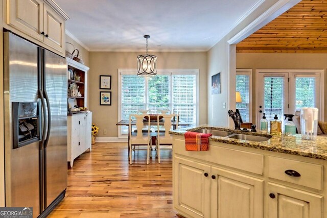 kitchen featuring stainless steel refrigerator with ice dispenser, crown molding, an inviting chandelier, light wood-type flooring, and light stone counters