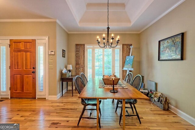 dining area featuring light hardwood / wood-style floors, crown molding, a notable chandelier, and a raised ceiling