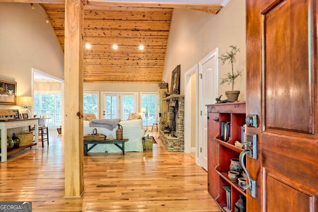 interior space with light hardwood / wood-style floors, high vaulted ceiling, wooden ceiling, and a stone fireplace