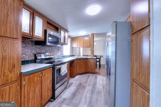 kitchen with appliances with stainless steel finishes, decorative backsplash, and light wood-type flooring