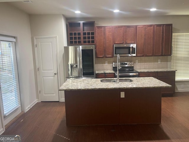 kitchen with dark hardwood / wood-style floors, stainless steel appliances, backsplash, and a center island with sink