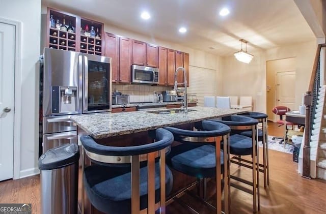 kitchen featuring dark wood-type flooring, appliances with stainless steel finishes, a kitchen island with sink, and backsplash