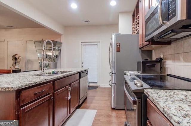 kitchen featuring decorative backsplash, appliances with stainless steel finishes, light stone countertops, light wood-type flooring, and sink