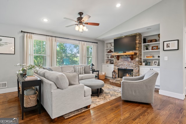 living room featuring ceiling fan, a stone fireplace, built in features, dark hardwood / wood-style floors, and vaulted ceiling