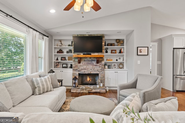 living room with a stone fireplace, ceiling fan, vaulted ceiling, and hardwood / wood-style flooring