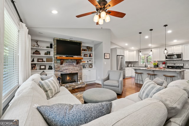 living room with vaulted ceiling, ceiling fan, wood-type flooring, built in features, and a fireplace