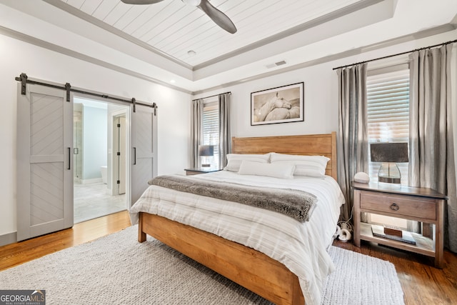 bedroom featuring a raised ceiling, multiple windows, ceiling fan, and hardwood / wood-style floors