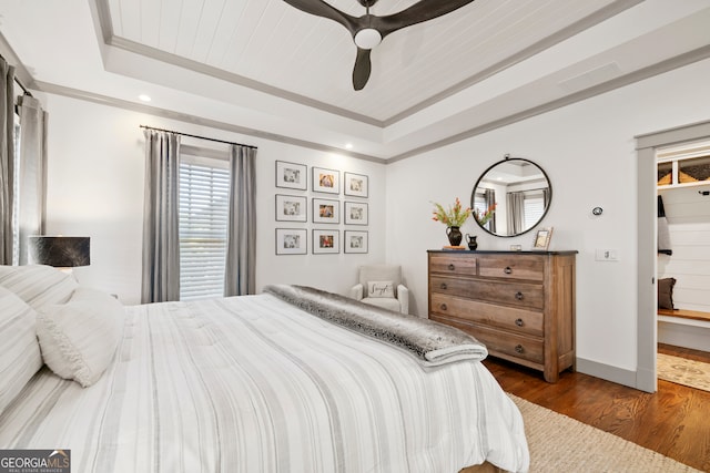 bedroom featuring dark hardwood / wood-style floors, ceiling fan, crown molding, and a tray ceiling