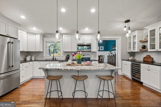 kitchen with appliances with stainless steel finishes, white cabinetry, hanging light fixtures, and beverage cooler