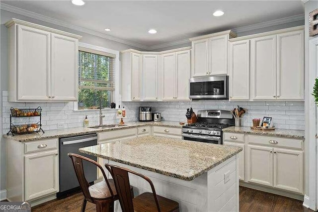 kitchen featuring sink, light stone countertops, a center island, white cabinets, and appliances with stainless steel finishes