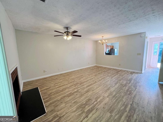 unfurnished living room with hardwood / wood-style flooring, ceiling fan with notable chandelier, and a textured ceiling