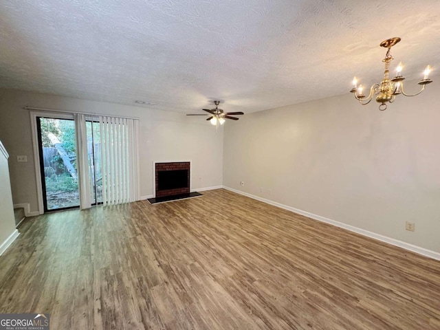 unfurnished living room featuring a brick fireplace, hardwood / wood-style flooring, ceiling fan with notable chandelier, and a textured ceiling