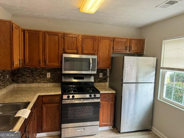 kitchen featuring sink, a textured ceiling, stainless steel appliances, light hardwood / wood-style floors, and decorative backsplash