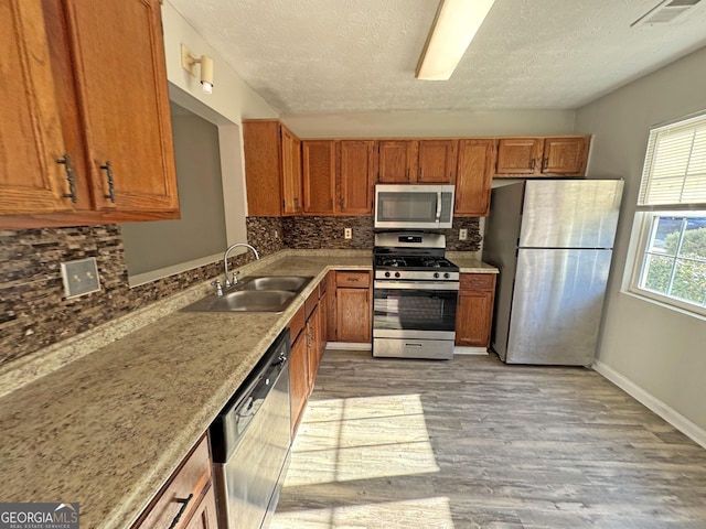 kitchen featuring light hardwood / wood-style flooring, sink, backsplash, a textured ceiling, and stainless steel appliances