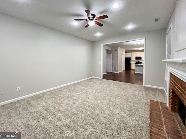 unfurnished living room featuring dark colored carpet, a textured ceiling, ceiling fan, and a brick fireplace