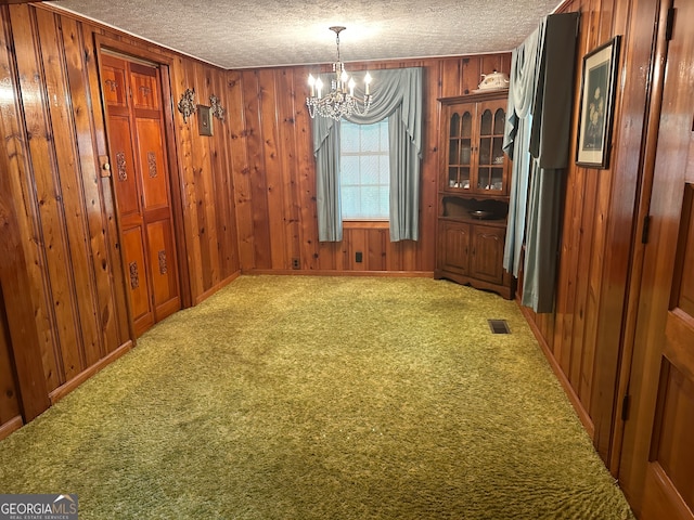 unfurnished dining area with a textured ceiling, carpet floors, an inviting chandelier, and wood walls